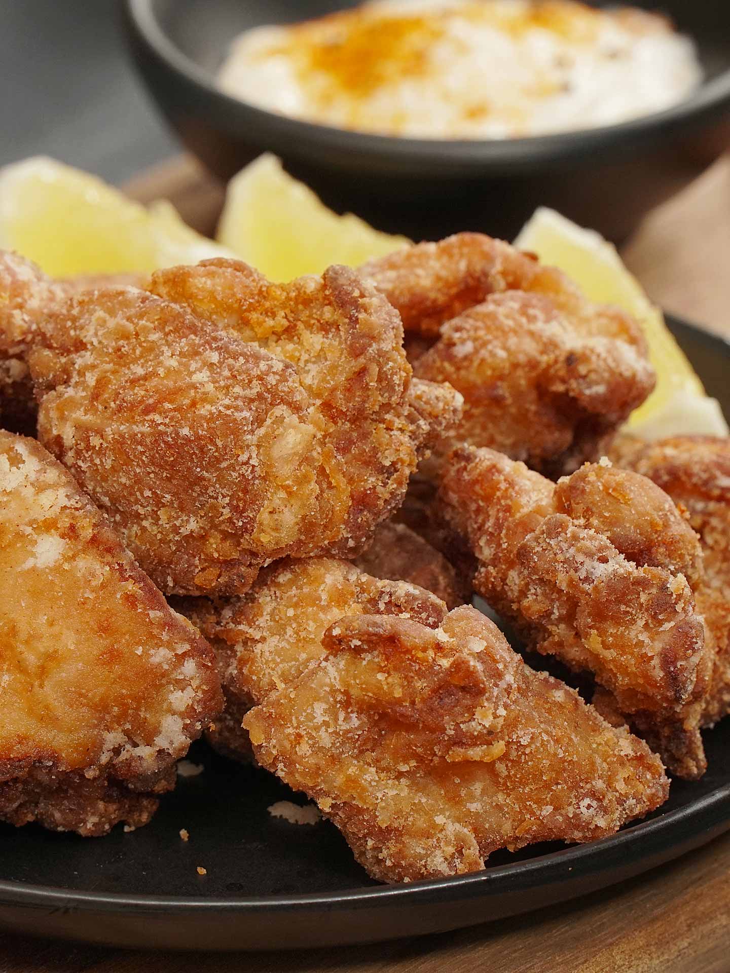 A black plate containing Japanese Karaage chicken pieces, garnished with lemon wedges.