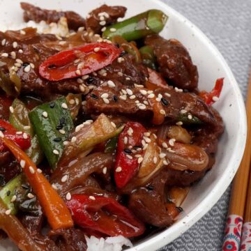 A white bowl with korean style spicy beef stir fry on the bed of white rice.