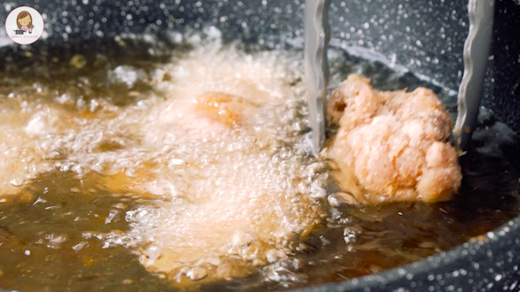 A black pot containing hot oil frying chicken wings. 