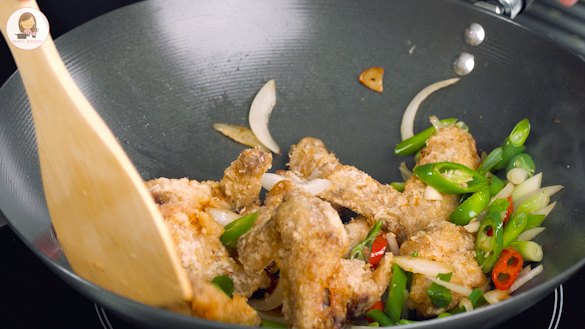A black wok containing, fried chicken wings and vegetables.