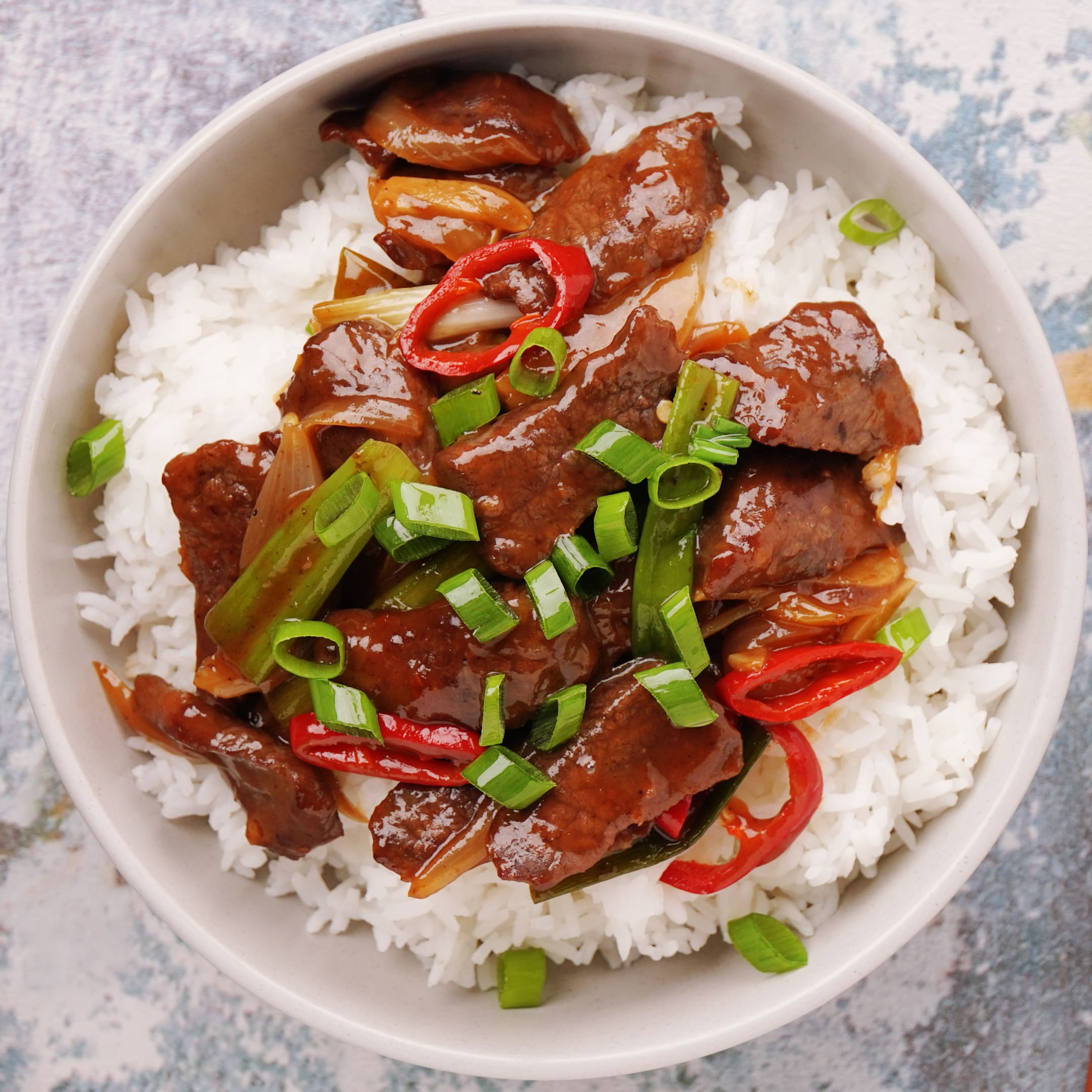 A bowl of rice with stir fry Mongolian beef with spring onion and chilli slices. 