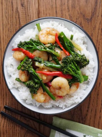 Stir fry prawn and broccoli on the bed of white rice in the white colour bowl with black colour chop stick.