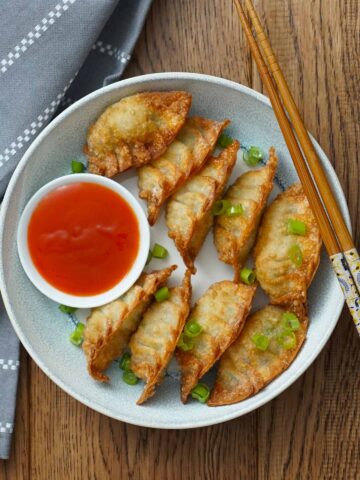crispy deep fried dumpling and a small chilli dipping sauce put together in the bowl with chop stick on the right side of the bowl.