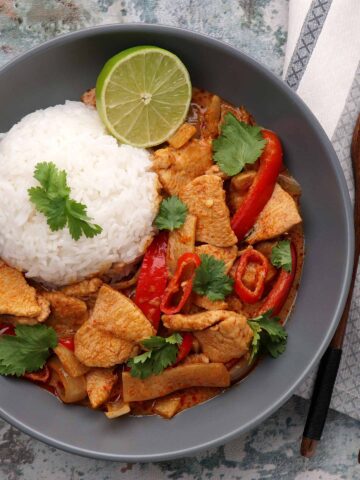 A round shape of white rice next to thai style red curry and half sliced of lime on the grey colour plate.