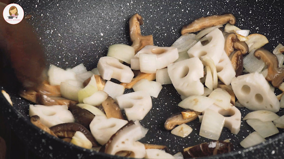 A black wok containing, lotus root, mushroom, and onions.