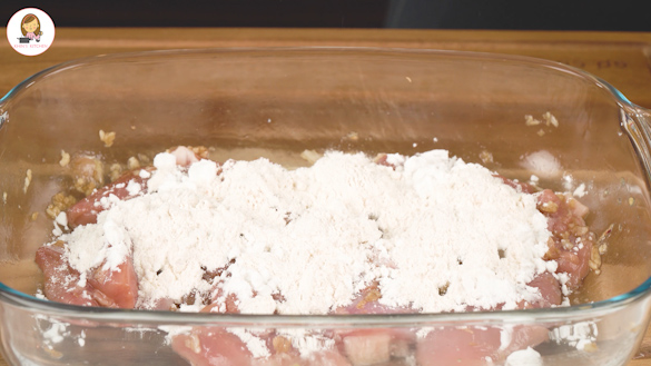 A clear bowl containing marinated chicken with corn starch and plain flour mixture.