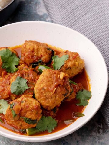 A white bowl full of Asian style Chicken balls curry and sprinkle with coriander.
