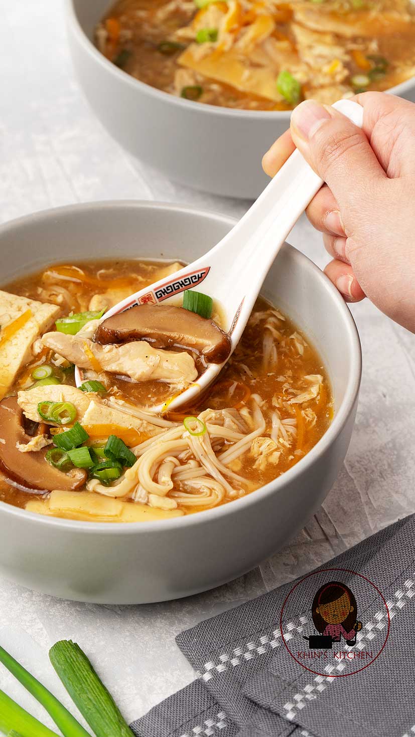 A grey bowl containing, Chinese hot and sour soup with mushrooms, tofu, spring onions an chicken strips.