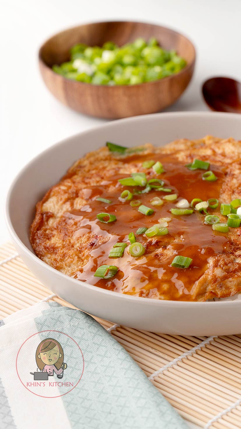 A white plate containing Chinese Egg Omelette with brown foo young sauce and spring onions.