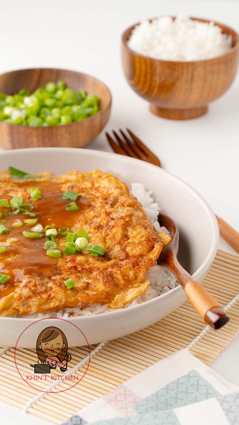 A white plate containing golden egg omelette with gravy, spring onions and wooden spoon on the side. 