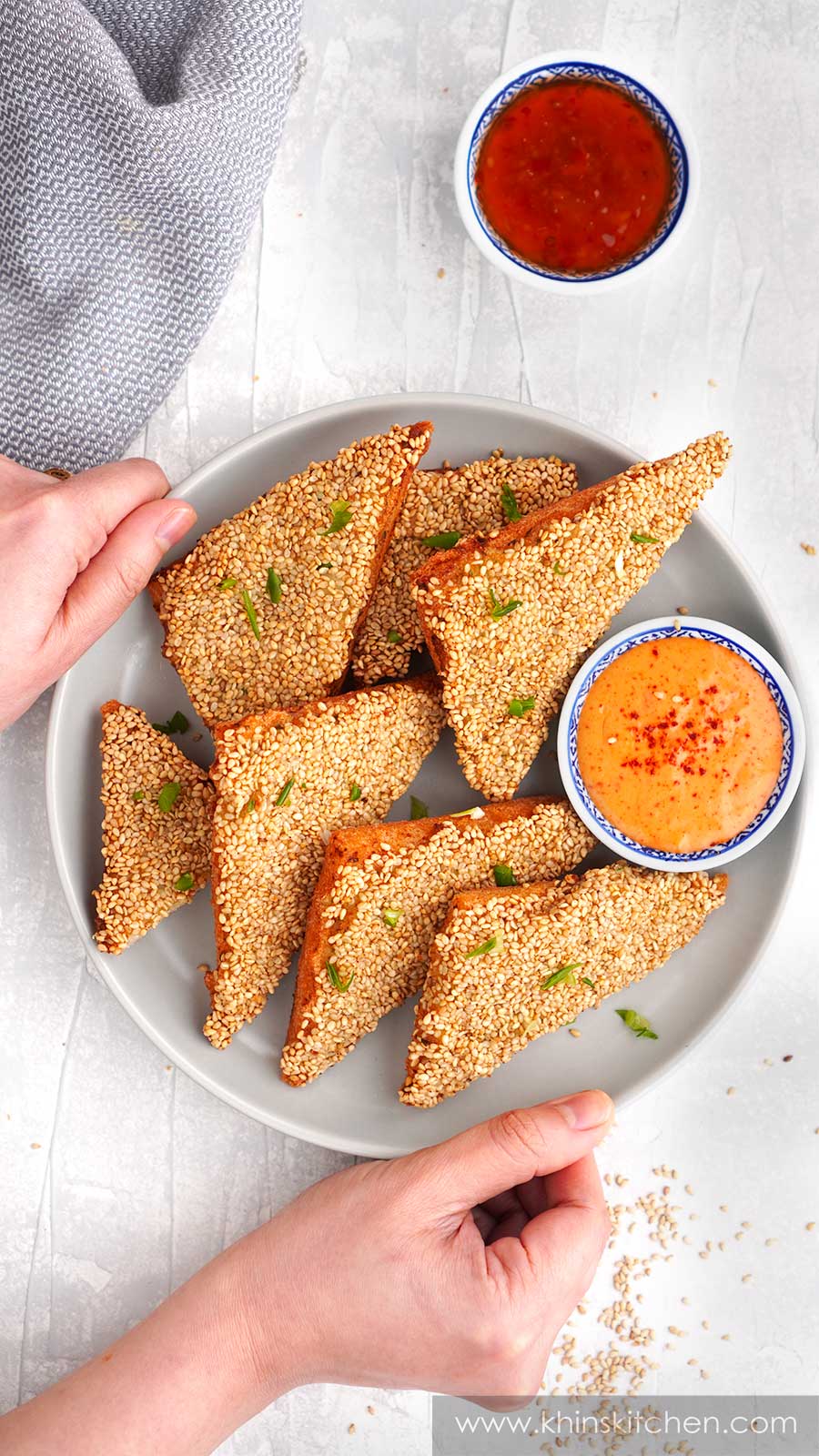 A grey plate containing fried sesame prawn toast with spicy mayonnaise. Sweet chilli dipping sauce on the side. 