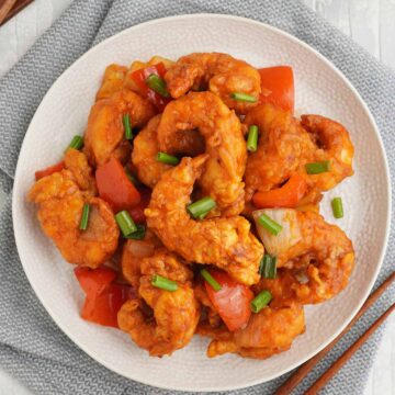 white plate full of sweet and sour prawns with wooden chop stick and a bowl of rice in wooden bowl.