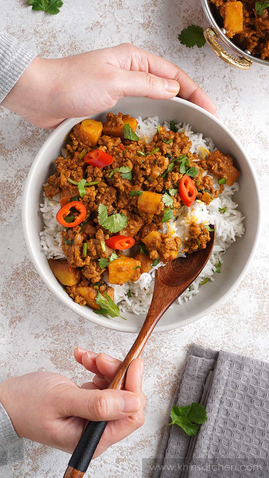 Ground beef curry,  cooked basmati rice in a cream colour bowl. Wooden spoon holding rice and minced beef. 