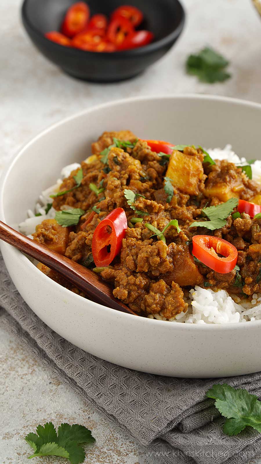 Close up shot of minced beef, potato cubes, chilli slices in a cream bowl. Wooden spoon in the bowl. 