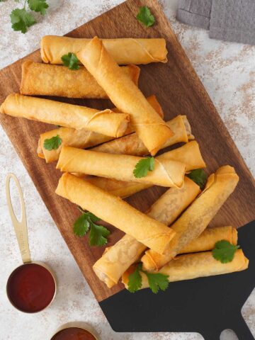 Thirteen spring rolls on the serving wooden boards with chilli dipping sauce.