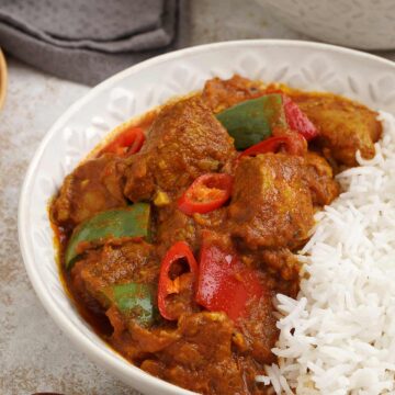 Close up photo of chicken jalfrezi and white rice with wooden chop stick in the foreground.