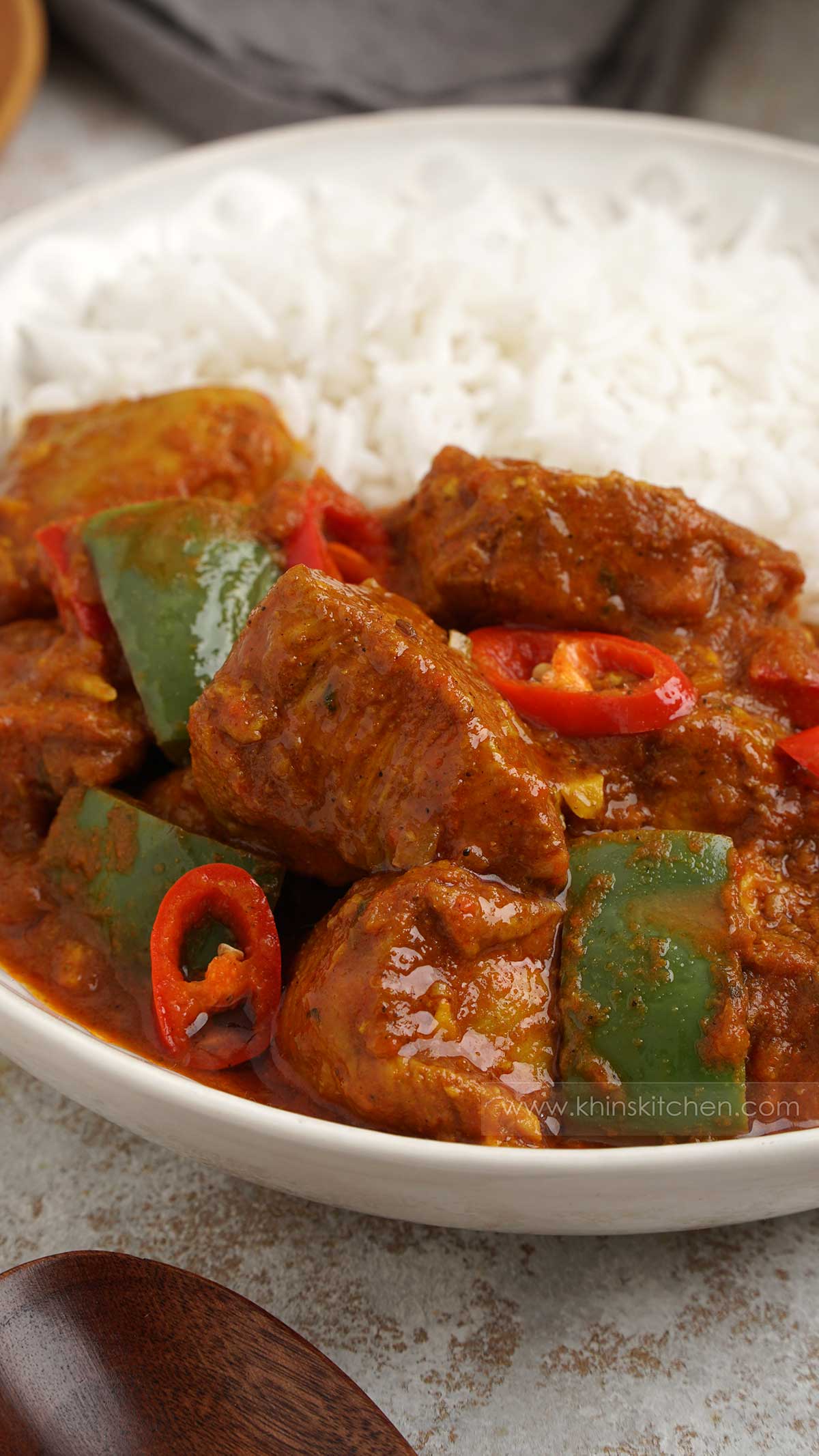 Close up shot of chicken curry with peppers and chilli slices, white rice at the background. 