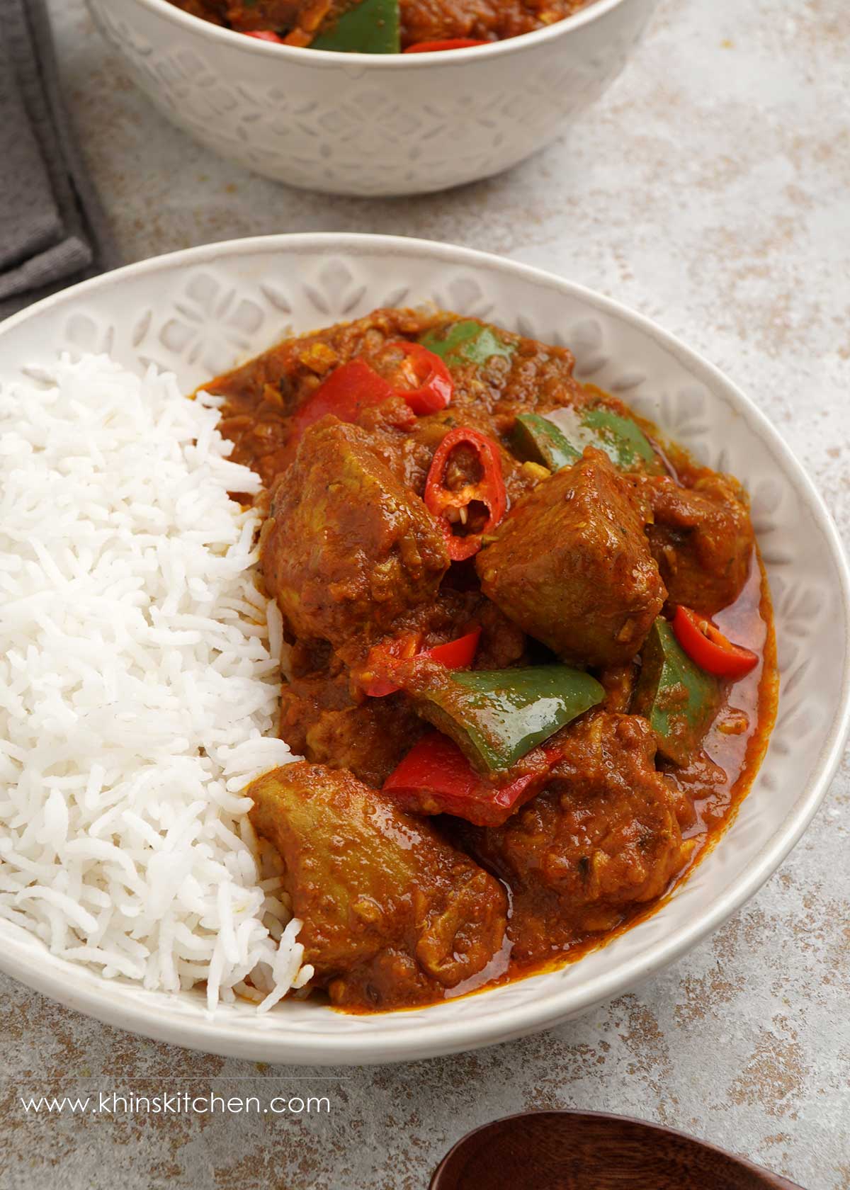 Close up photo of rice and chicken curry with peppers, in a white plate.