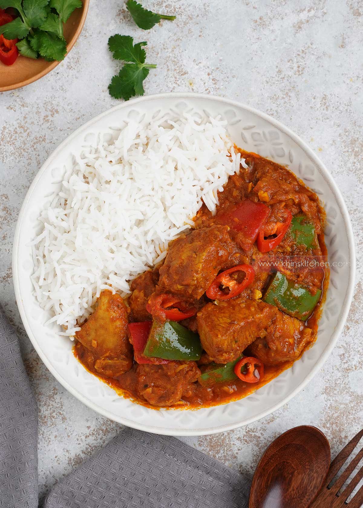 A white plate containing plain rice and chicken jalfrezi curry displayed on the white table. 