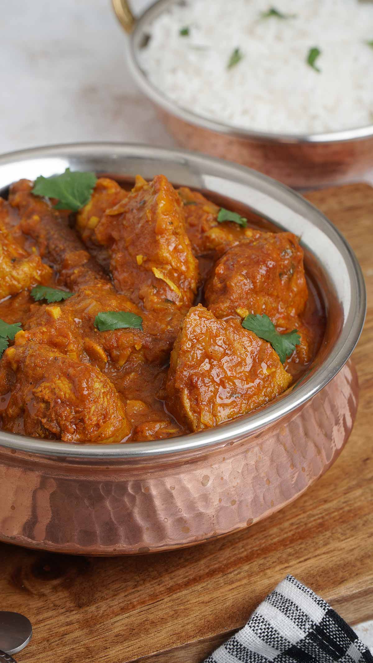 A steel bowl filled with chicken curry on the wooden serving board.