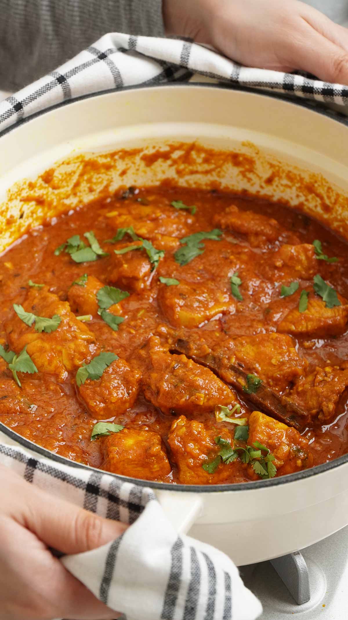 2 hands holding the casserole pot filled with Indian chicken madras curry.