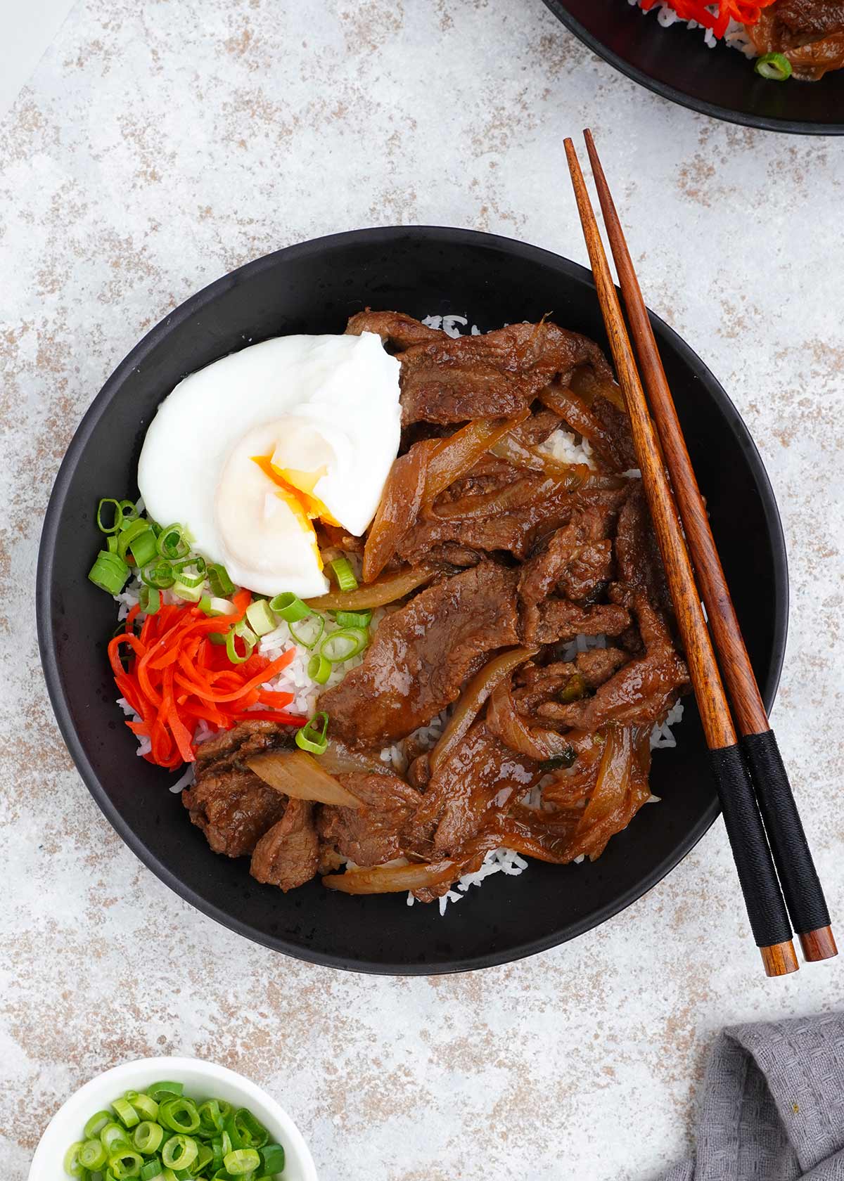 A black bowl filled with japanese beef with wooden chop side on the side.