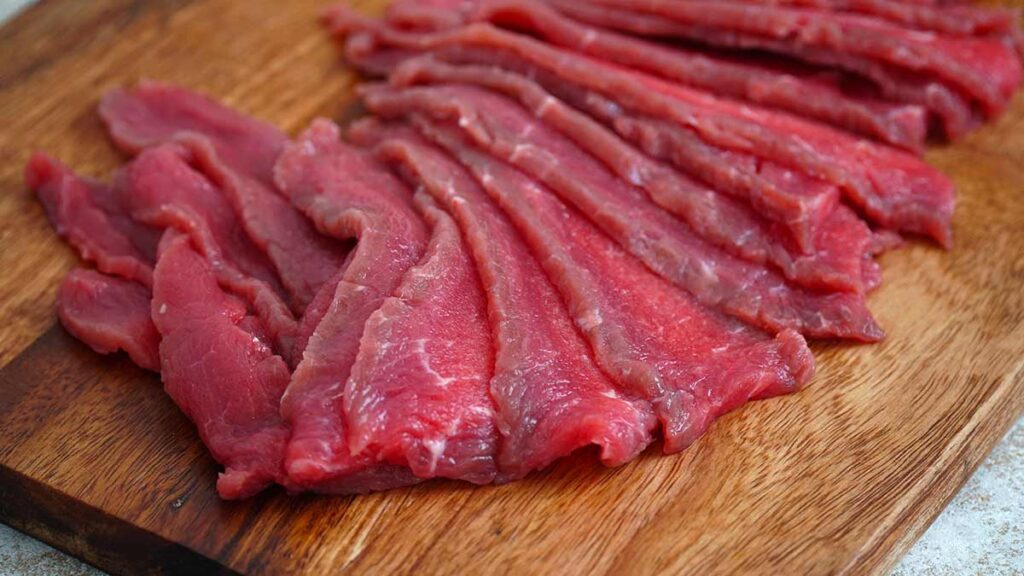 Thin slices beef on the wooden chopping board.