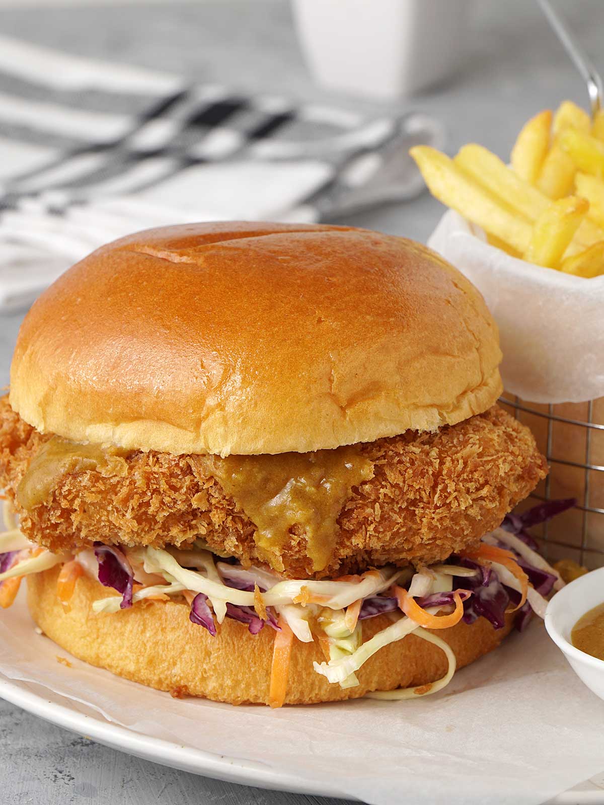 burger on the plate with a small bowl of curry sauce and chip basket in the background.