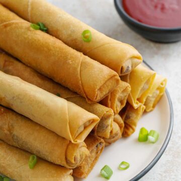 spring rolls ont the plate in the foreground and chilli dipping sauce in the background.