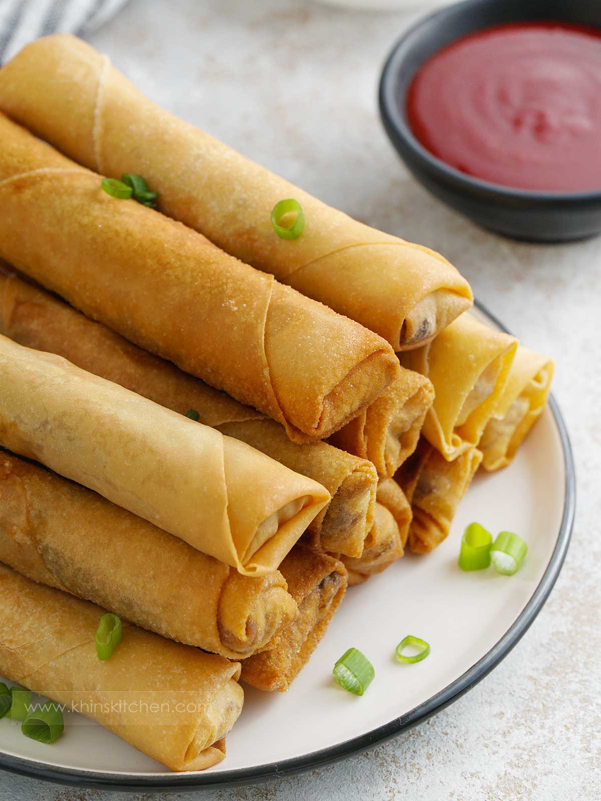 spring rolls ont the plate in the foreground and chilli dipping sauce in the background.