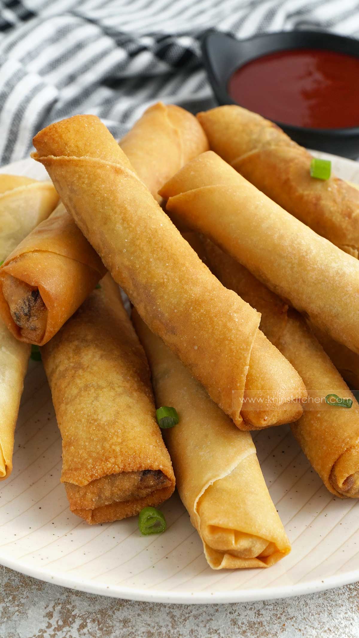 spring rolls stacking each other and a small bowl of chilli sauce in the background.