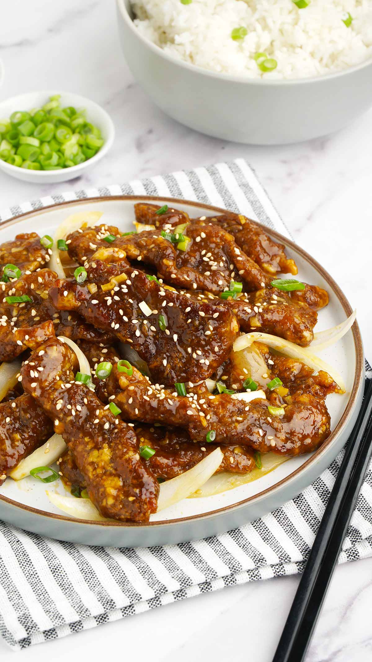 chinese style crispy orange beef on the white plate with black chop stick on the side.