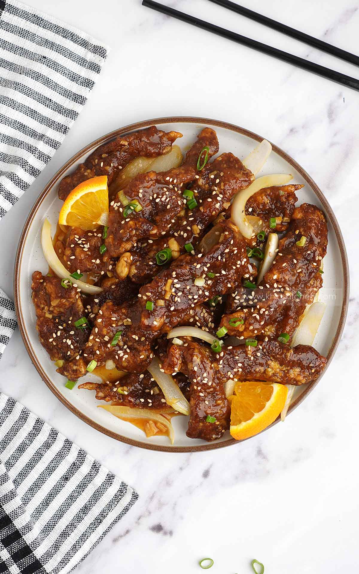 Orange beef in the white plate and black and white tea towels on the side with black wooden chop stick.