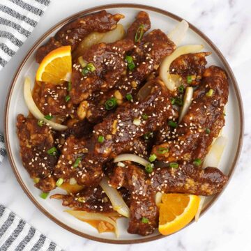 A plate full of crispy shredded beef and black and white strip napkin on the left side.