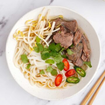 a white bowl filled with chinese noodles soup.