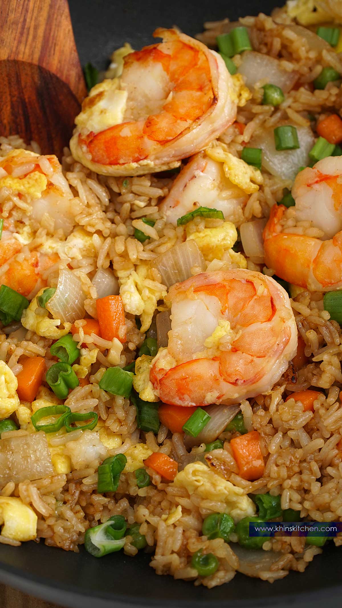 A close up view of rice, shrimp in the wok with wooden spatula.