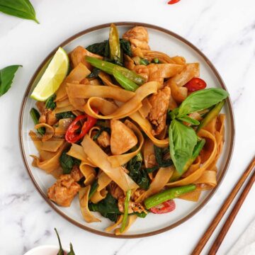 a plate full of thai noodles stir fry with wooden chopstick at the side.