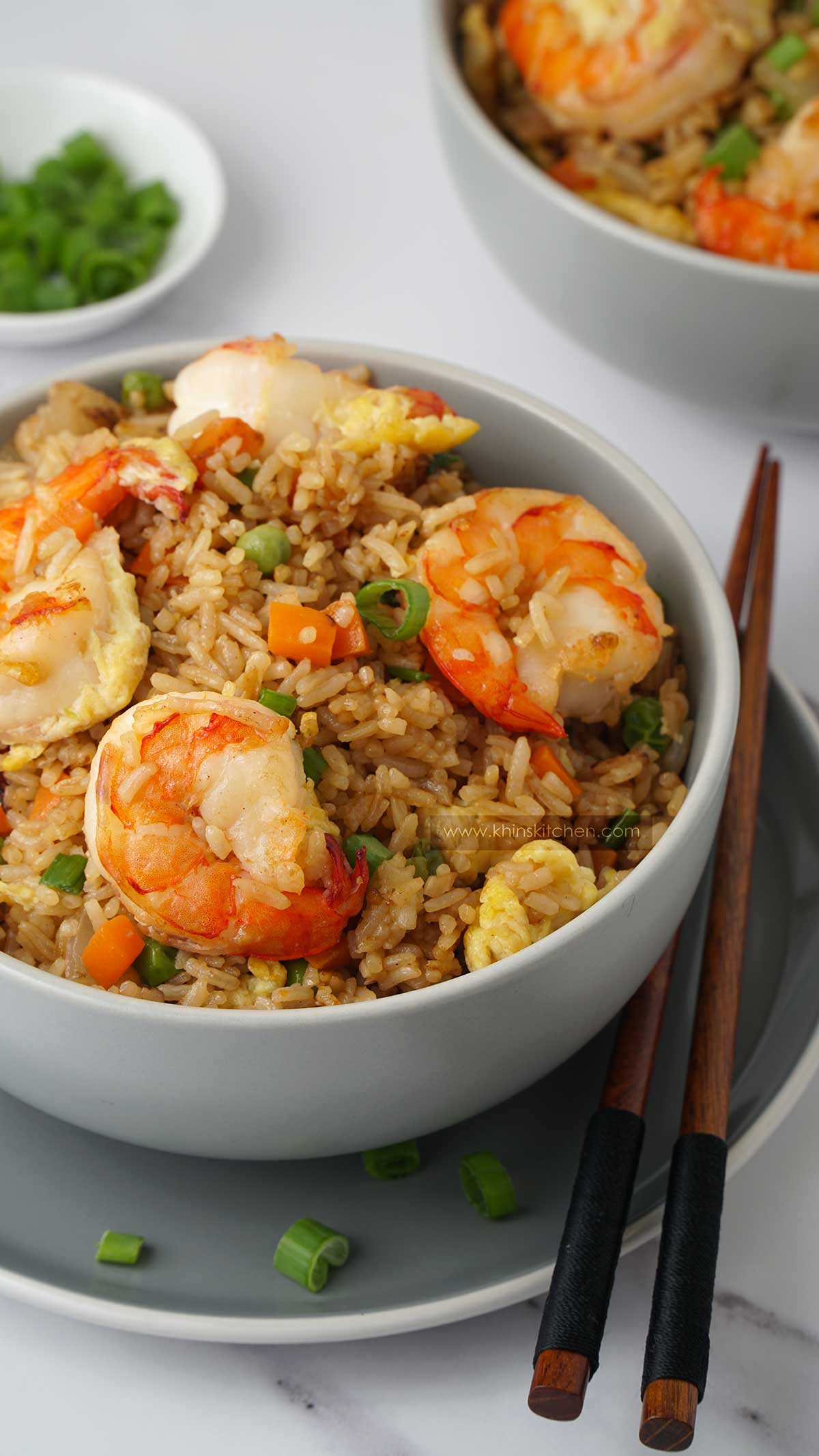 Rice, king prawns, vegetables in the grey bowl with wooden chop stick on the side.