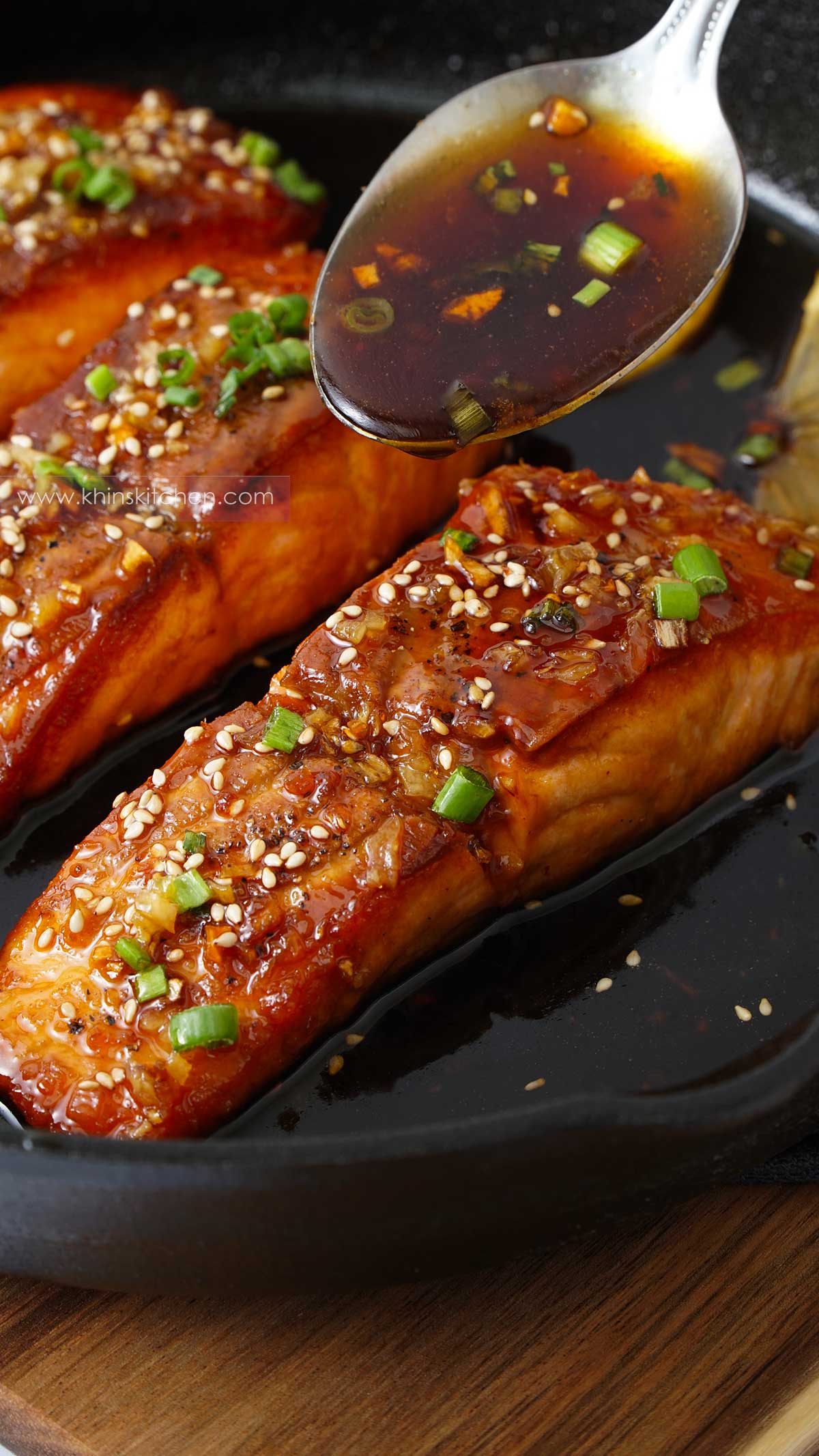 A skillet filled honey garlic salmon and sauce drizzling from spoon.