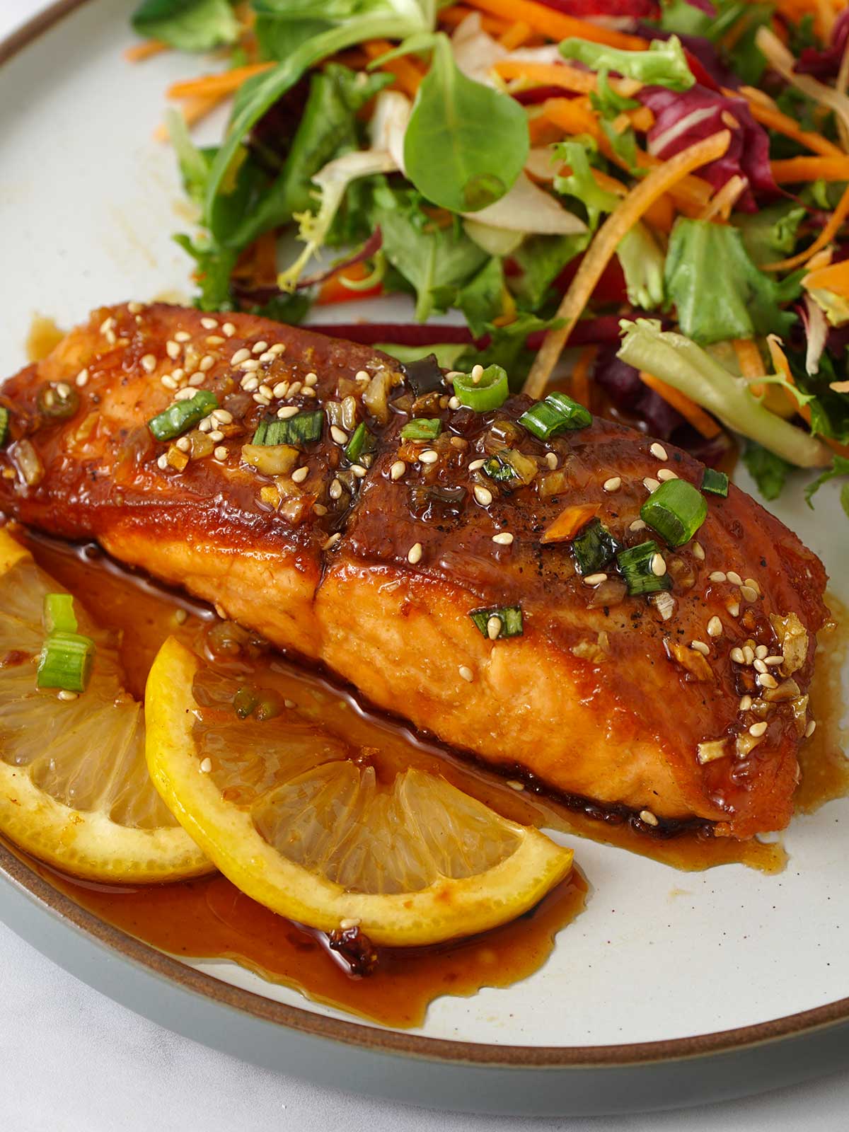 Honey salmon salmon, with two slices of lemon and a side of salad on the white plate.