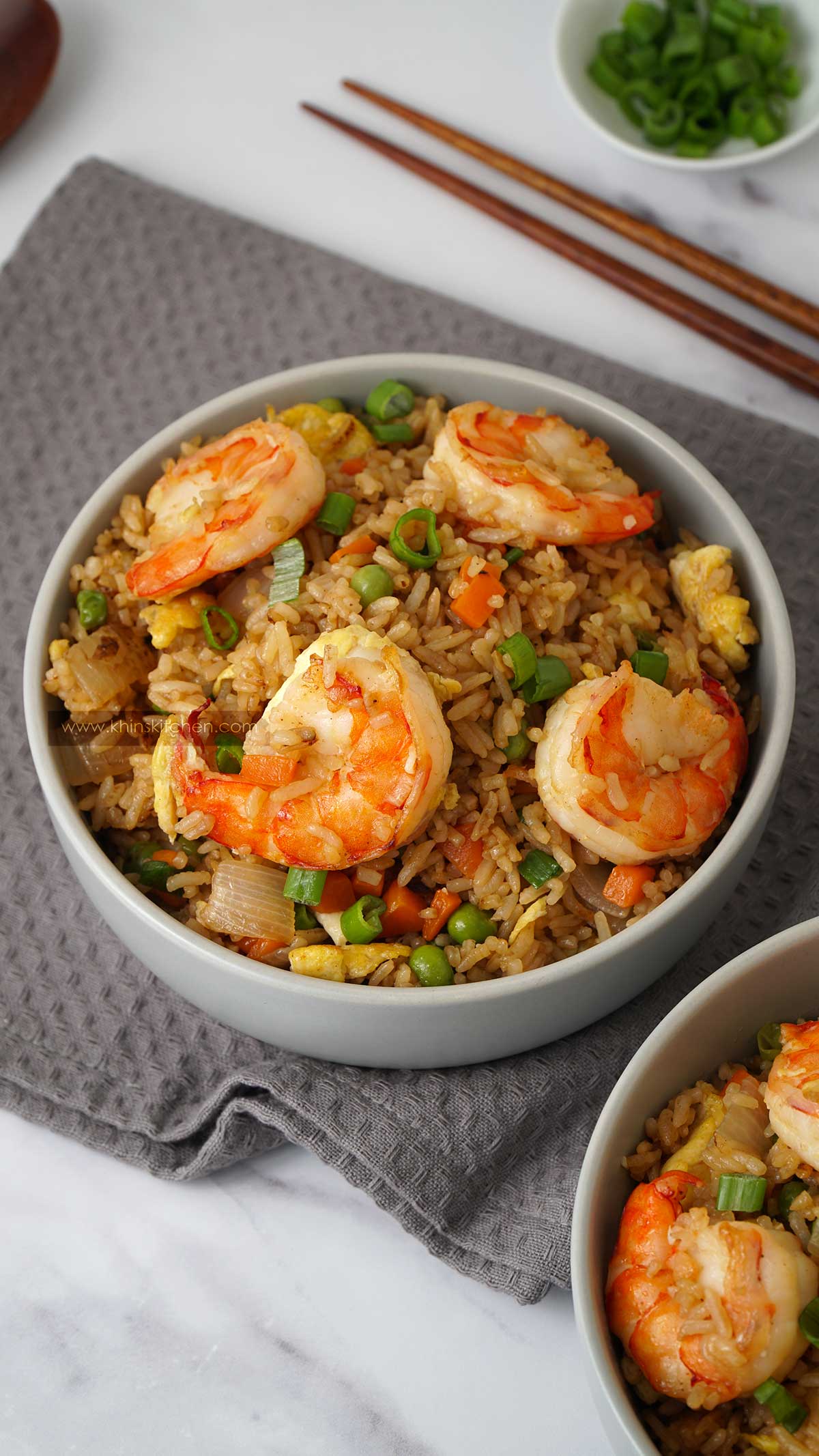 A bowl full of rice, prawns, vegetables on the grey tea towel and a wooden chopstick in the background.