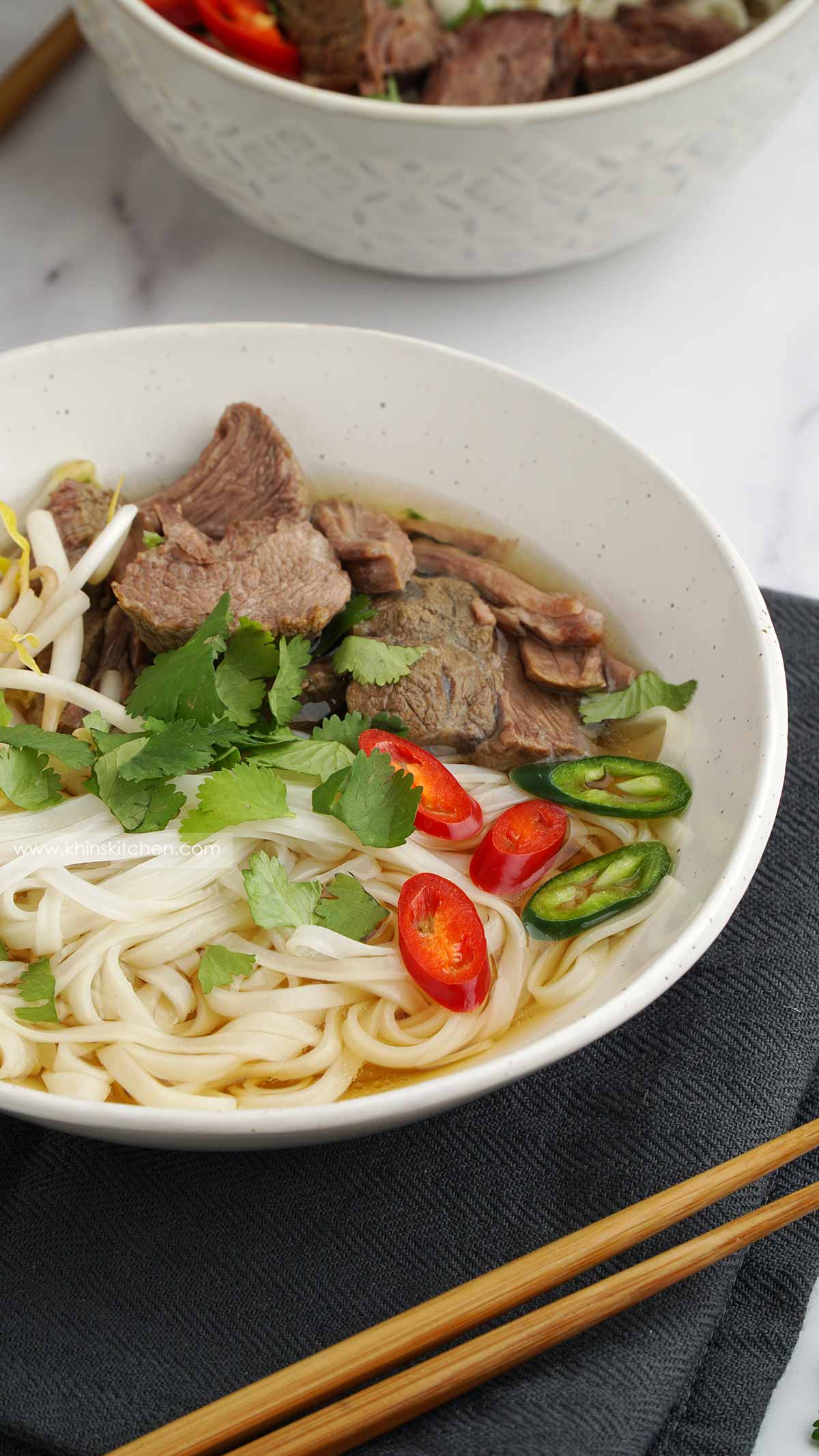 a white bowl filled with noodles soup on the black tea towel.