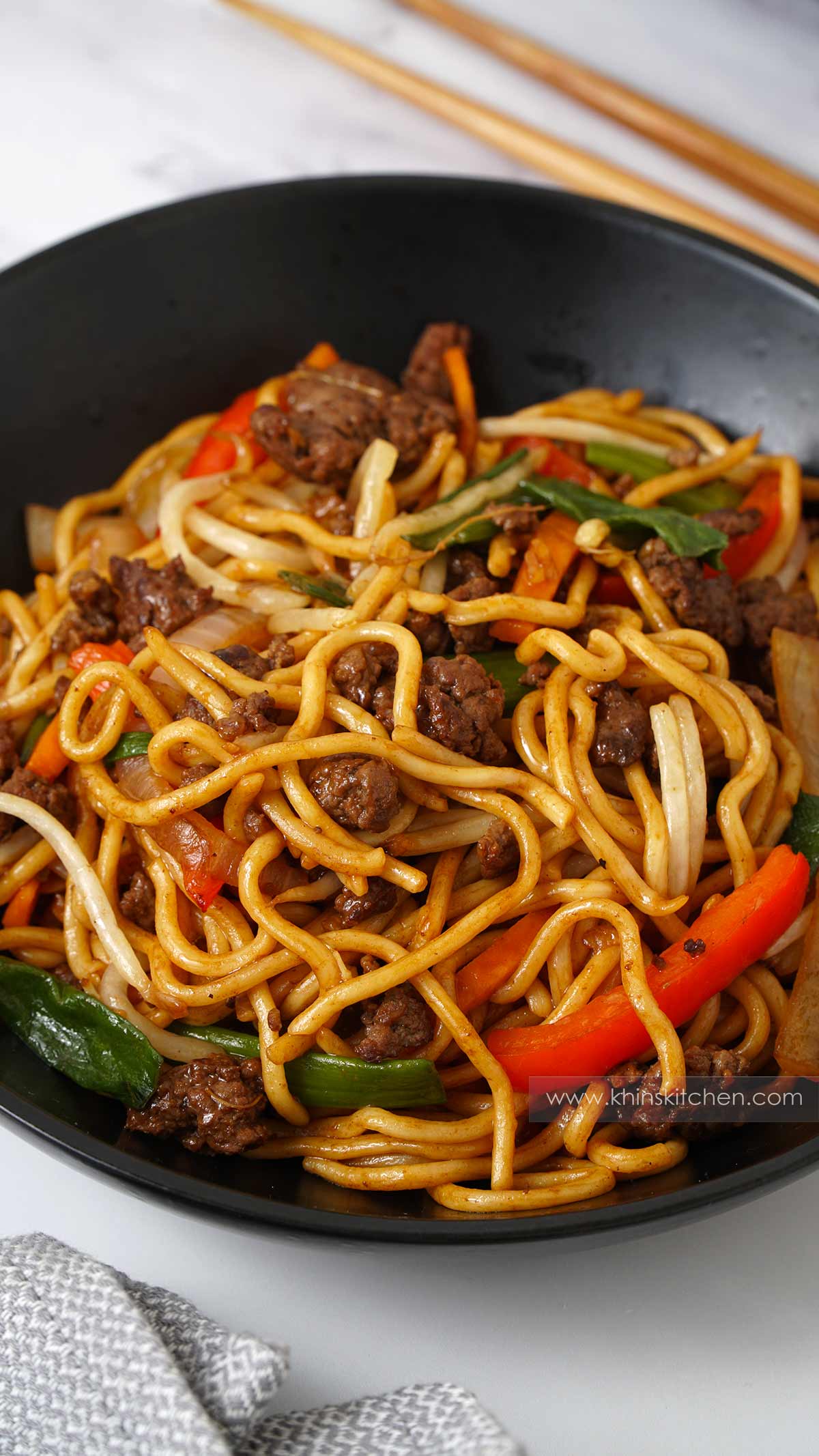 A black bowl containing stir fry noodles, sliced vegetables, ground beef.