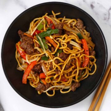 A black bowl containing stir fry noodles, ground beef, vegetables and beansprouts.