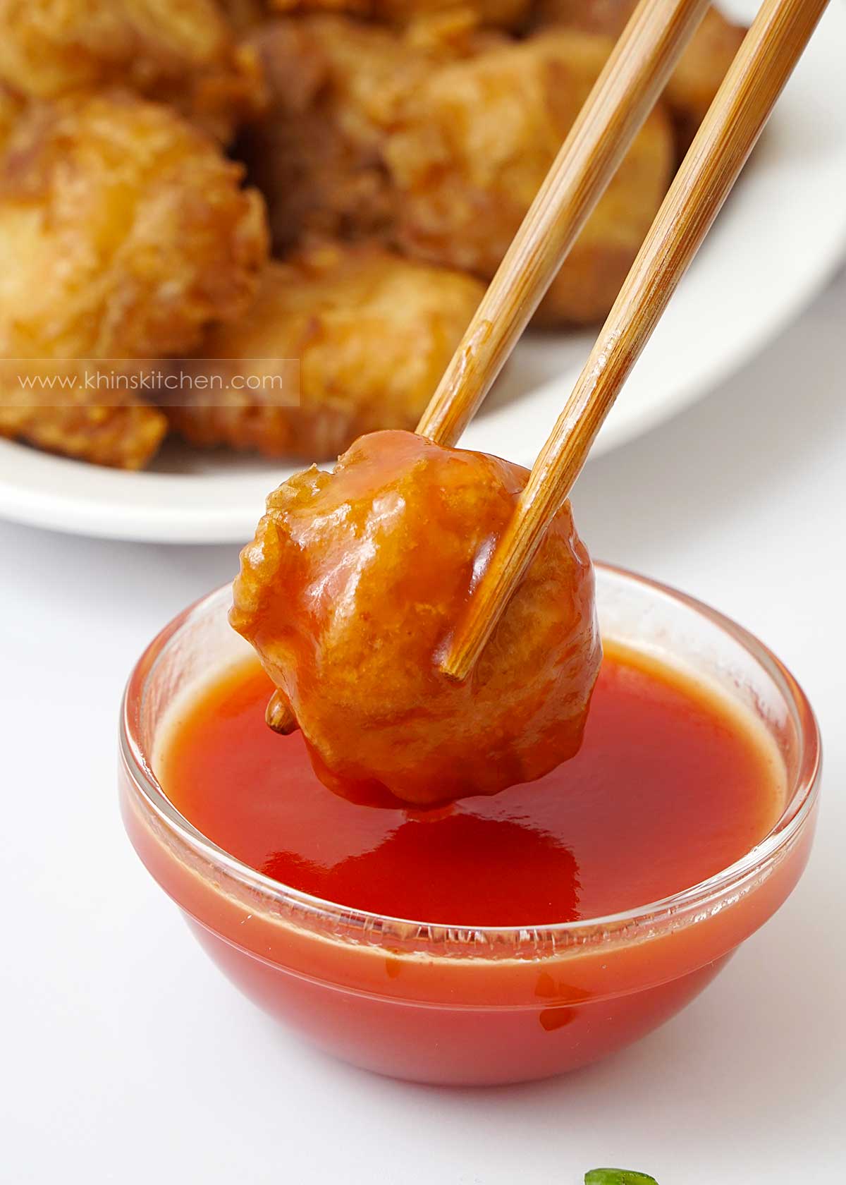  une baguette en bois tenant les boulettes de poulet trempe dans la sauce.