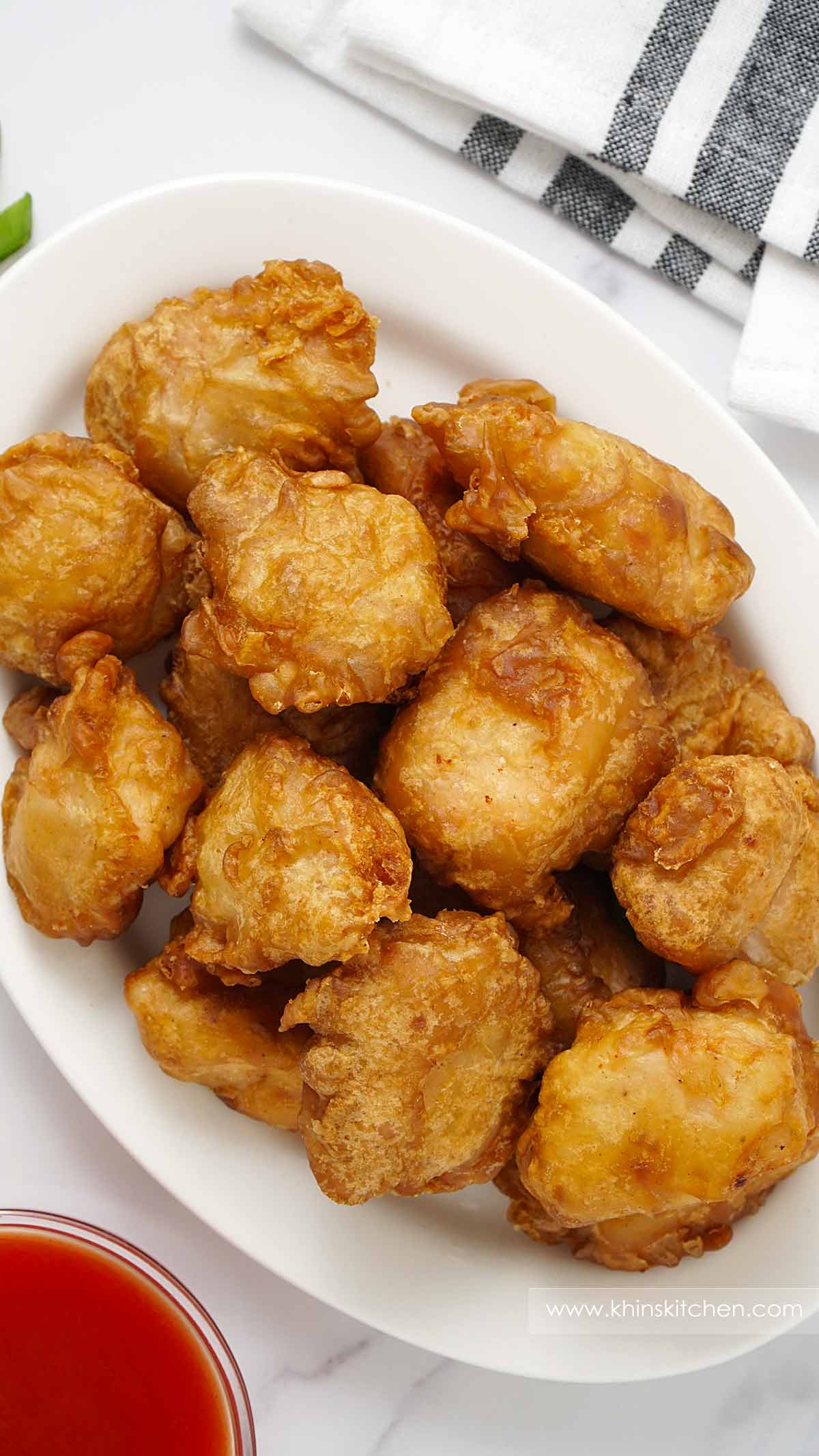 A white plate containing crispy chicken balls and a small dipping bowl with sweet and sour sauce.