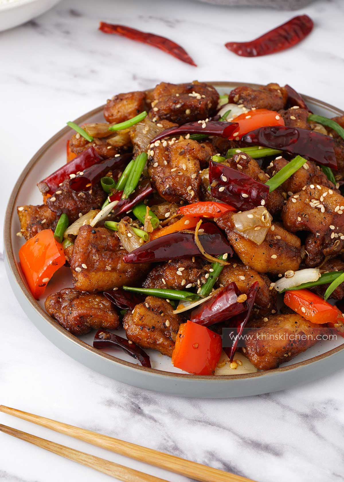 A white plate containing, stir fried chicken, onion, peppers, dry chillies, Sichuan peppercorns and sesame seeds.