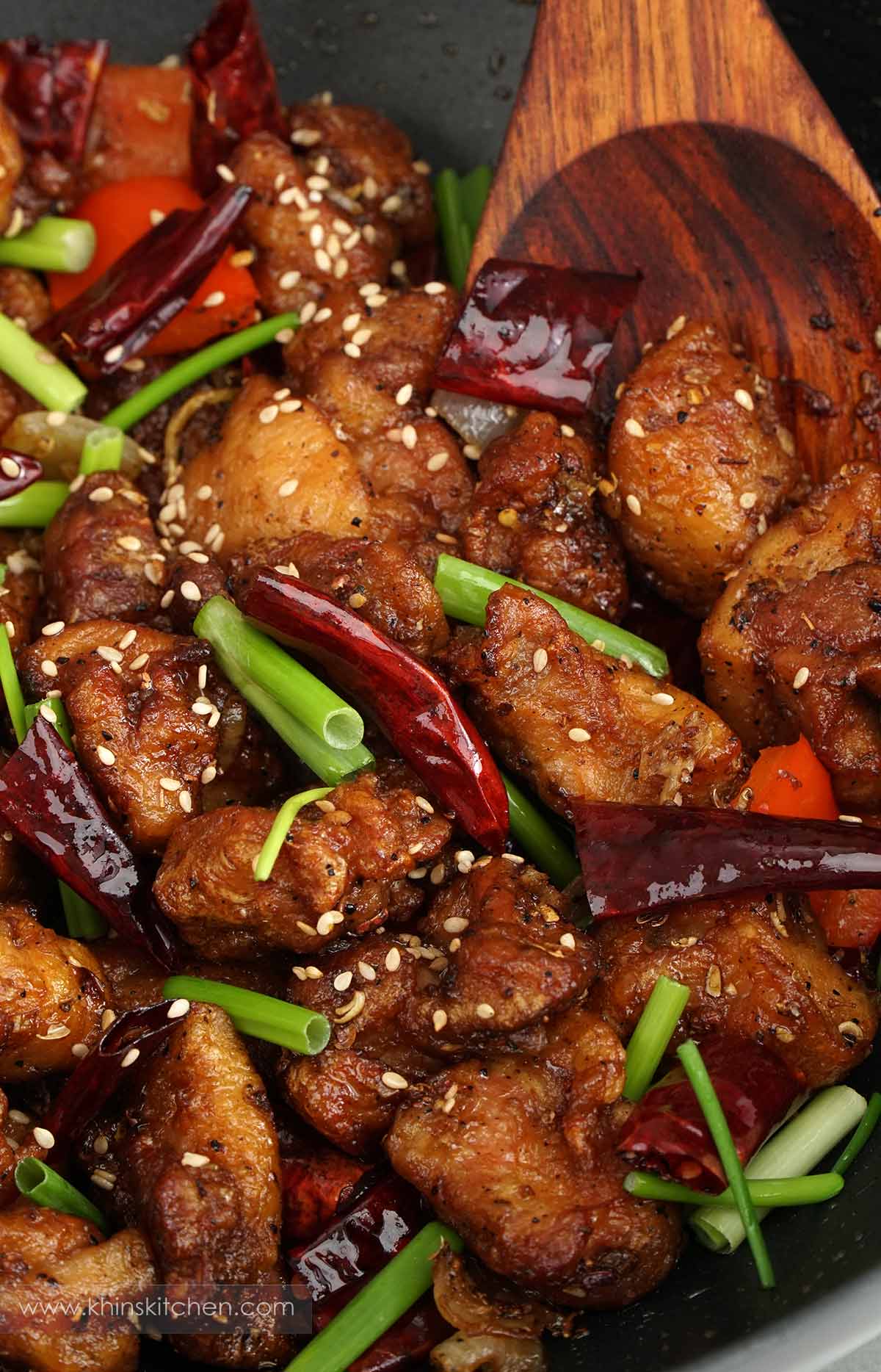 A skillet containing crispy fried chicken, stir fry vegetable and dried red chillies.