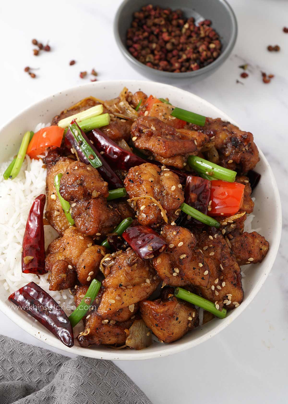 Spicy chinese chicken stir fry on top of the rice in the white bowl and grey tea towel at the side.