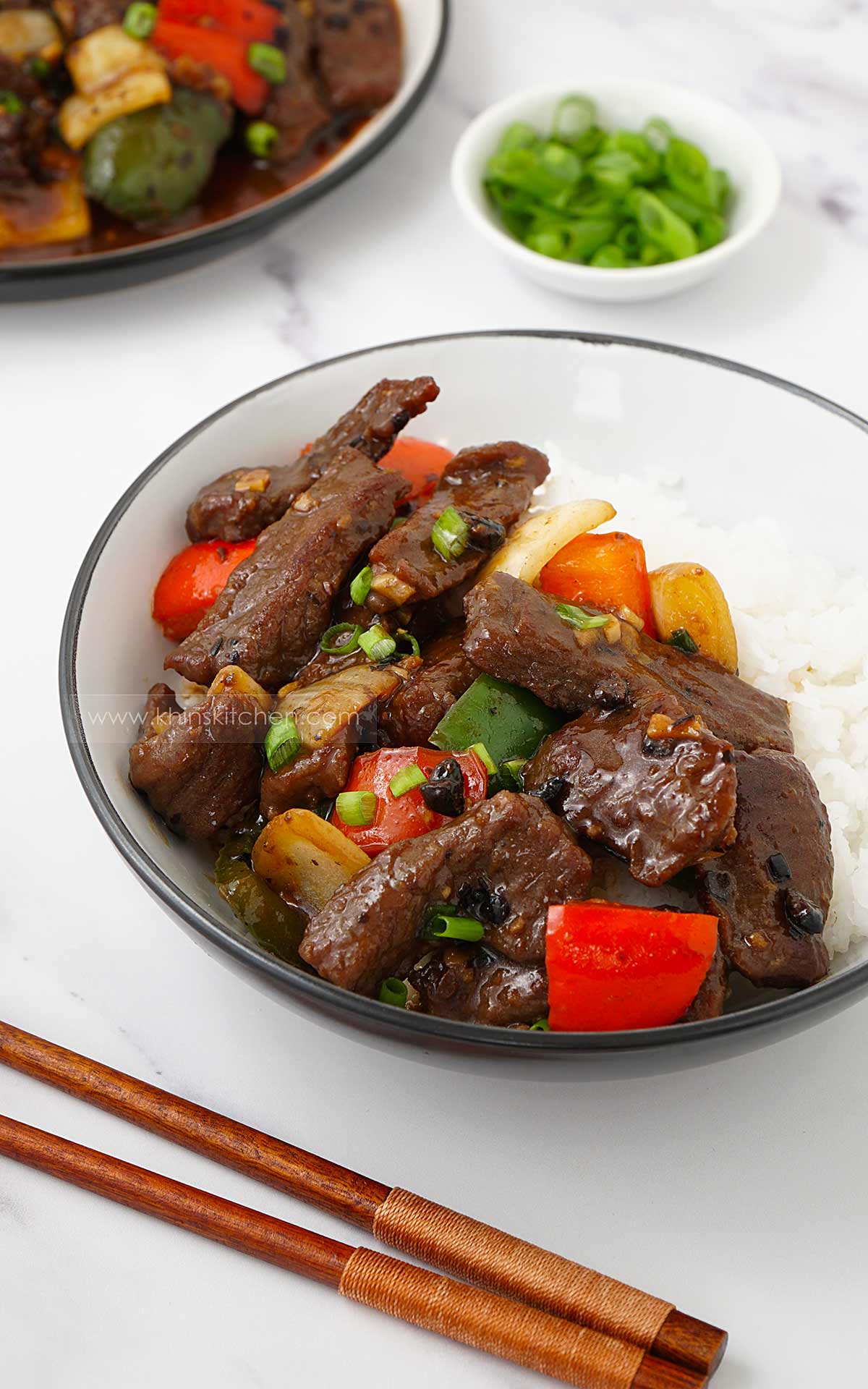 White bowl containing beef stir fry with vegetables and black bean sauce, over white rice.